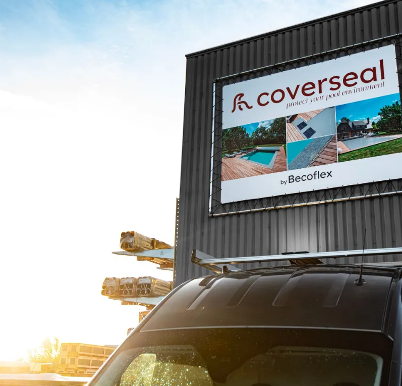Affiche "Coverseal" sur un bâtiment gris, avec des images de piscines, un ciel bleu et une voiture noire au premier plan.