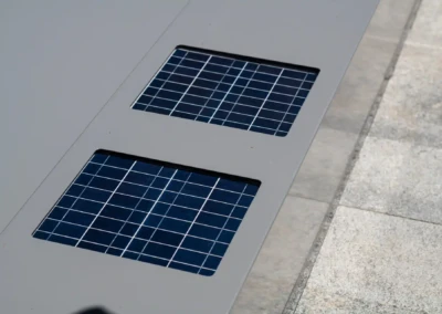 Deux panneaux solaires rectangulaires bleus encastrés dans une surface grise, bordée de dalles de pierre grise.