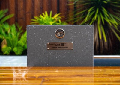 Panneau gris avec logo et texte "couverseal" sous la pluie, entouré de végétation verte et bordure en bois mouillé.