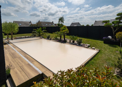 Piscine totalement sécurisée grâce à une couverture Coverseal beige, intégrée dans un jardin paysager avec végétation méditerranéenne.