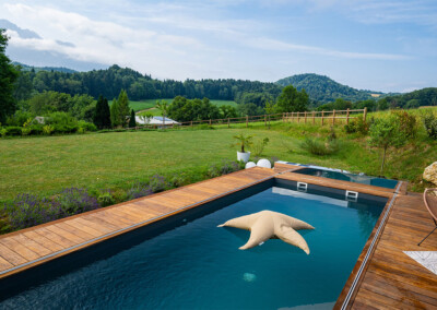 Piscine design avec terrasse en bois et vue panoramique sur la campagne et les collines environnantes.