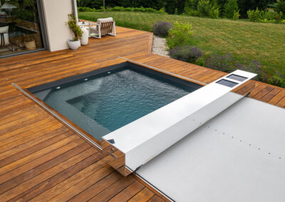 Piscine rectangulaire avec le modèle automatique en cours de fermeture, intégrée dans une terrasse en bois.