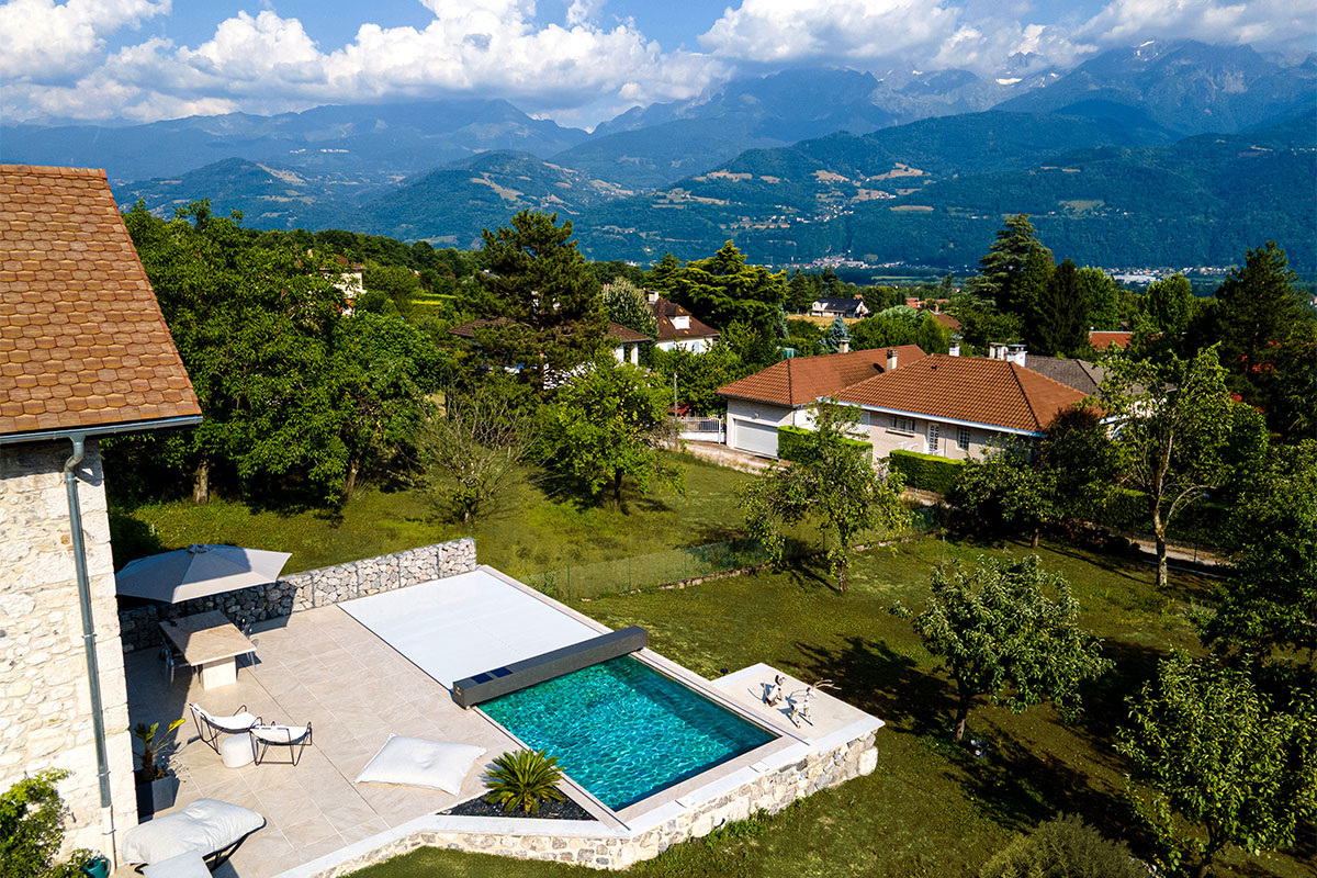 Vue aérienne d’une piscine moderne équipée d’une couverture Coverseal, intégrée à une terrasse en pierre, avec en arrière-plan les montagnes alpines.