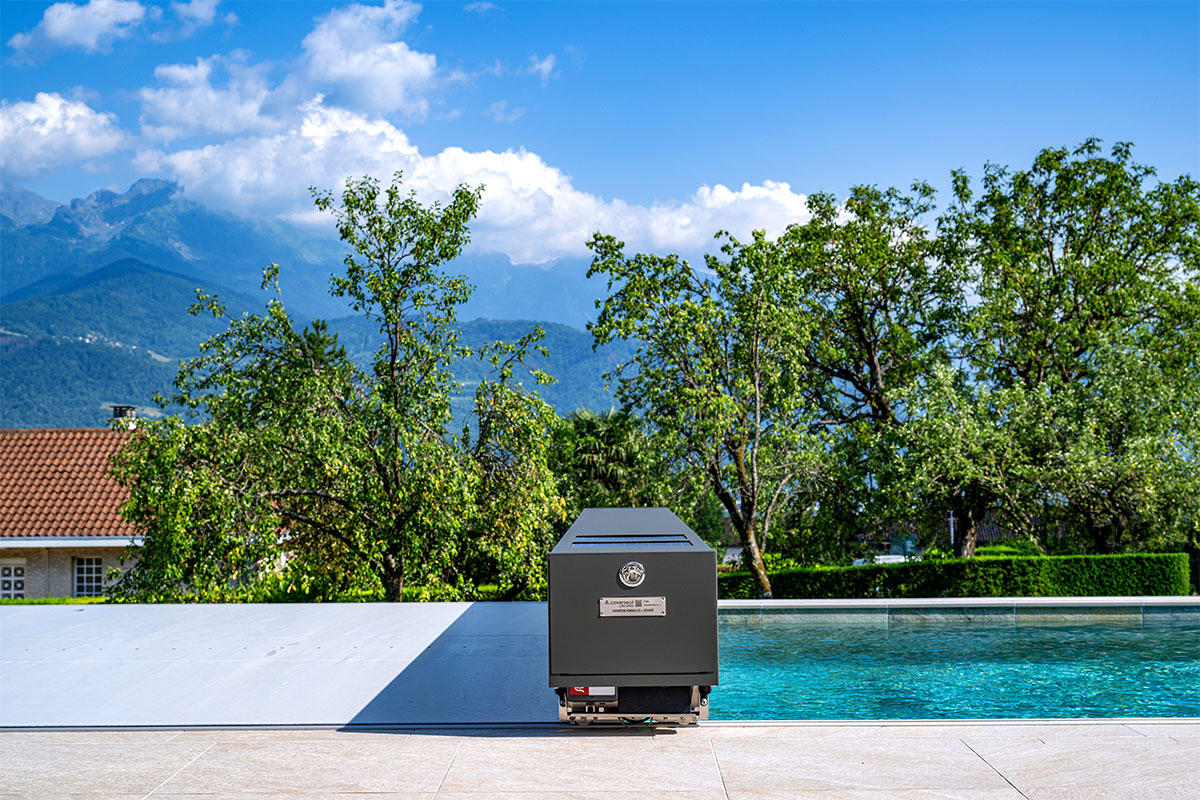 Couverture Coverseal fermée sur une piscine, avec boîtier de mécanisme gris et vue panoramique sur les montagnes et la verdure environnante.