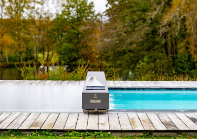 Piscine avec couverture Coverseal partiellement ouverte laissant apparaître une eau turquoise, dans un cadre naturel boisé.