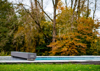 Piscine design équipée d’une couverture Coverseal, intégrée dans une terrasse en bois au cœur d’un grand jardin arboré.