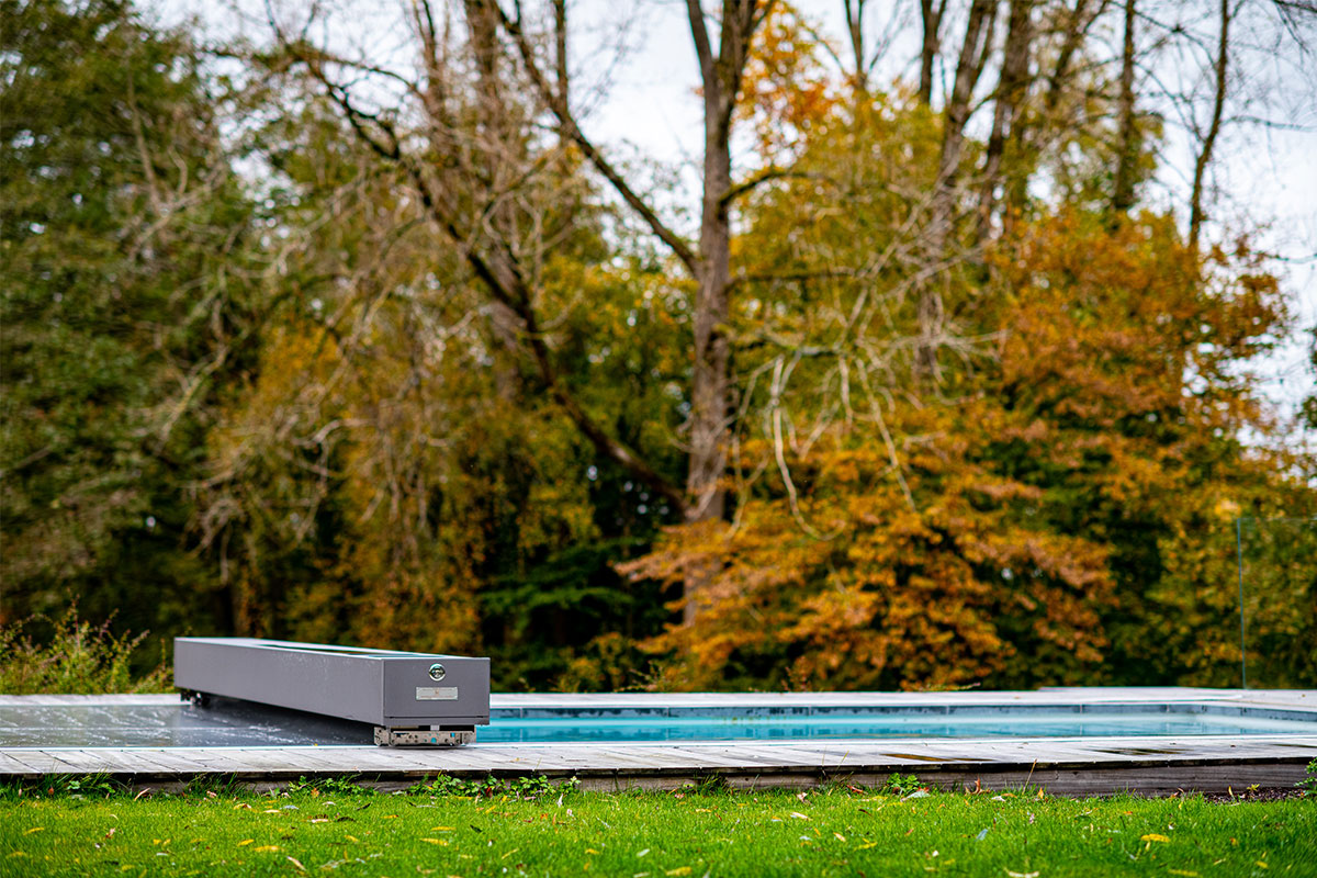 Piscine design équipée d’une couverture Coverseal, intégrée dans une terrasse en bois au cœur d’un grand jardin arboré.