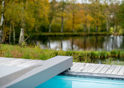 Détail du mécanisme Coverseal au bord d’une piscine, avec vue sur un étang naturel et une végétation automnale.